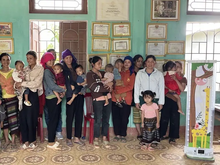 Caregivers and children waiting at a commune health station, with the prototype board standing at the right.